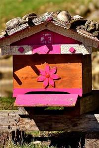 An Adorable Wooden Beehive with Pink Flowers in a Field Journal