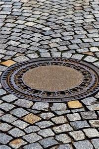 Manhole Cover on a Cobblestone Street Journal